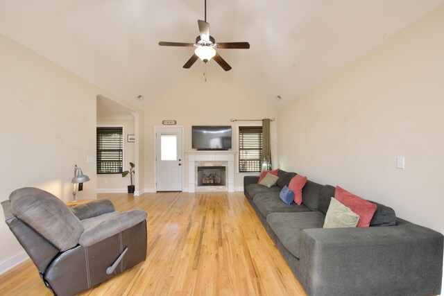 living room with wood-type flooring, ceiling fan, high vaulted ceiling, and a tile fireplace