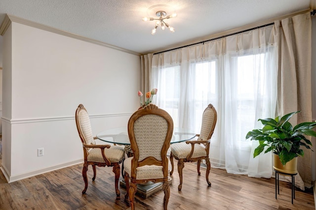 dining room with a textured ceiling, wood-type flooring, crown molding, and a notable chandelier