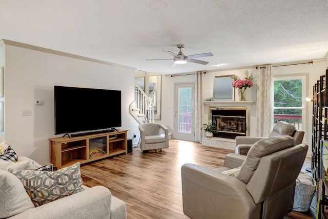 living room with light hardwood / wood-style flooring, ceiling fan, crown molding, and a textured ceiling