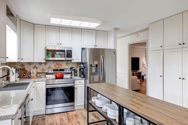 kitchen featuring sink, light hardwood / wood-style flooring, stainless steel appliances, decorative backsplash, and crown molding