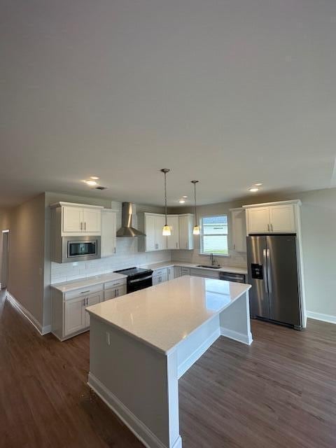 kitchen with white cabinets, appliances with stainless steel finishes, wall chimney exhaust hood, and a center island