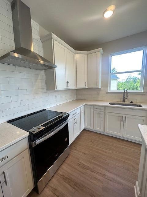 kitchen featuring wall chimney exhaust hood, white cabinets, electric stove, and sink