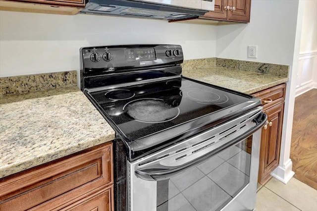 kitchen with light tile patterned floors, stainless steel range with electric cooktop, and light stone counters