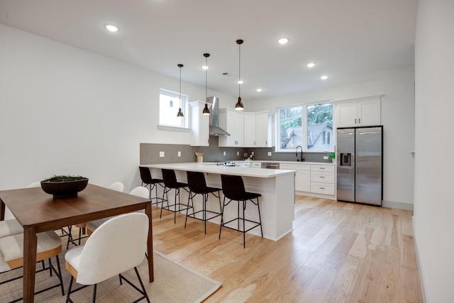 kitchen with a kitchen breakfast bar, tasteful backsplash, wall chimney exhaust hood, stainless steel refrigerator with ice dispenser, and a peninsula
