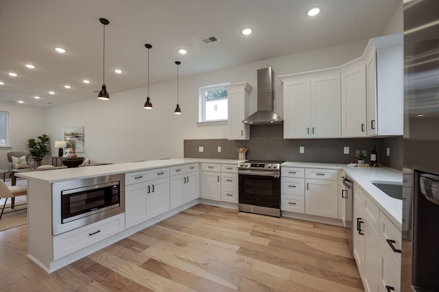 kitchen featuring stainless steel appliances, visible vents, a peninsula, wall chimney range hood, and light countertops