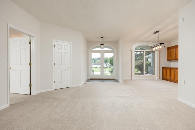 unfurnished living room featuring light carpet, a textured ceiling, and french doors