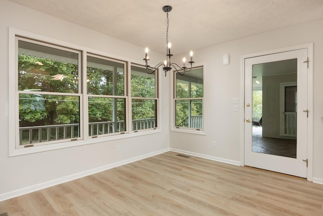 unfurnished dining area with a textured ceiling, light hardwood / wood-style flooring, and a notable chandelier