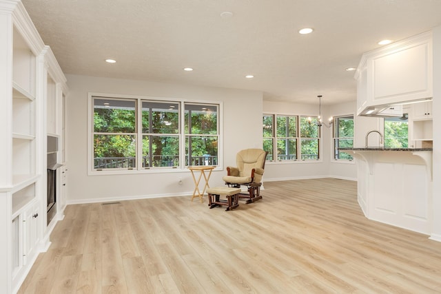 sitting room featuring a notable chandelier, light wood-type flooring, and a textured ceiling