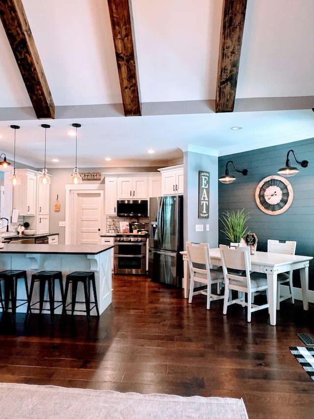 kitchen with white cabinetry, a breakfast bar area, beamed ceiling, stainless steel appliances, and decorative light fixtures