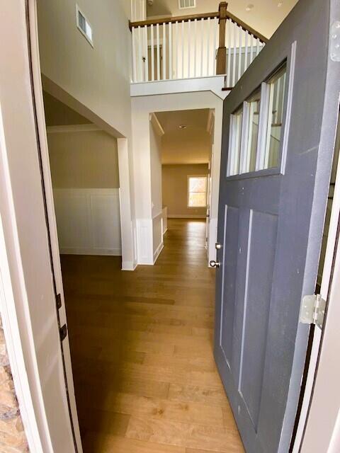 hall with light wood finished floors, wainscoting, a towering ceiling, and visible vents