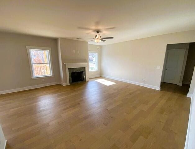 unfurnished living room with a ceiling fan, a fireplace, plenty of natural light, and wood finished floors