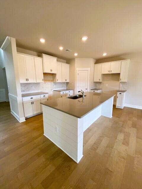 kitchen with a center island with sink, white cabinets, a sink, and wood finished floors