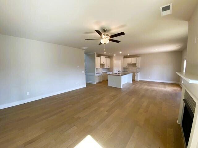 unfurnished living room with a fireplace, wood finished floors, visible vents, baseboards, and a ceiling fan