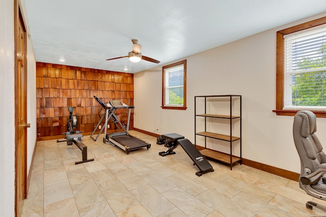 workout room featuring ceiling fan and wooden walls