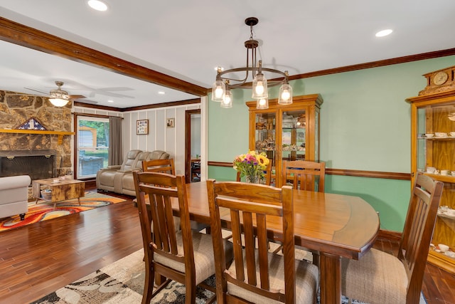 dining room with ceiling fan with notable chandelier, wood-type flooring, a fireplace, and crown molding