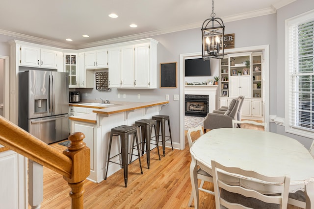 kitchen featuring pendant lighting, white cabinets, a fireplace, and stainless steel fridge with ice dispenser