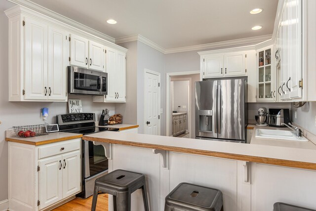 kitchen with a breakfast bar, white cabinetry, kitchen peninsula, and appliances with stainless steel finishes