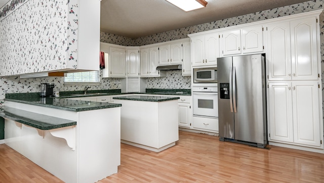 kitchen with white cabinets, light wood-type flooring, white appliances, and a kitchen island