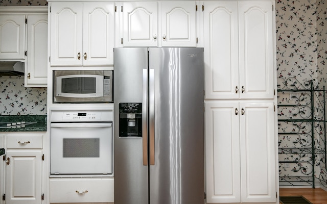 kitchen featuring appliances with stainless steel finishes, dark stone countertops, and white cabinetry