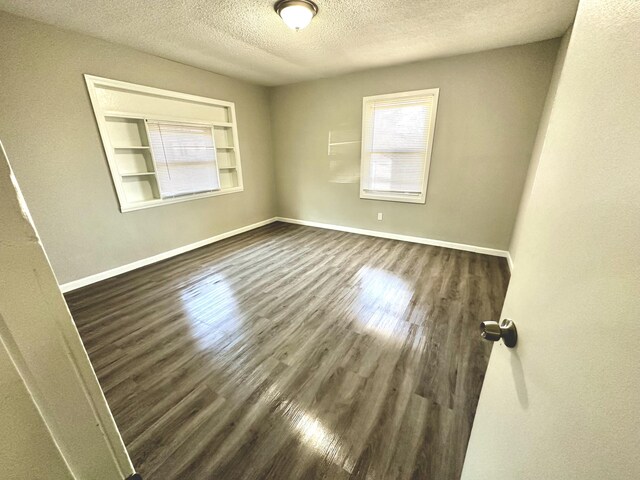 empty room featuring built in features, a textured ceiling, and dark hardwood / wood-style flooring