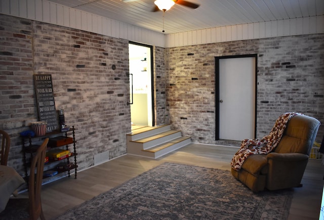 living area with wooden ceiling, wood-type flooring, ceiling fan, and brick wall