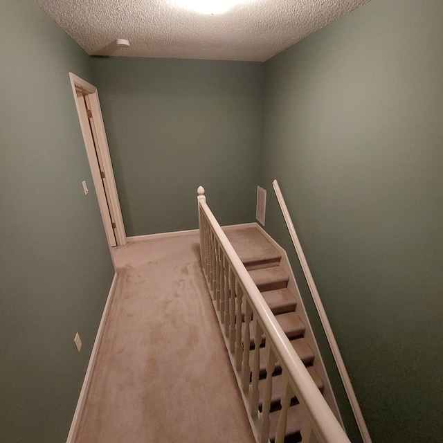 corridor with a textured ceiling and light colored carpet