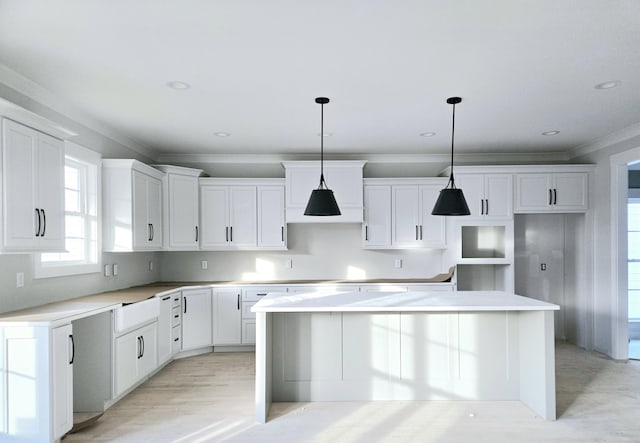 kitchen featuring white cabinets, ornamental molding, pendant lighting, light hardwood / wood-style flooring, and a center island