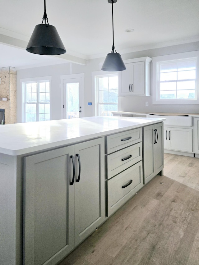 kitchen with white cabinetry, a large fireplace, light hardwood / wood-style flooring, and ornamental molding