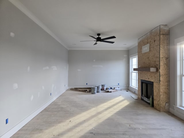 unfurnished living room featuring ceiling fan, a large fireplace, and ornamental molding