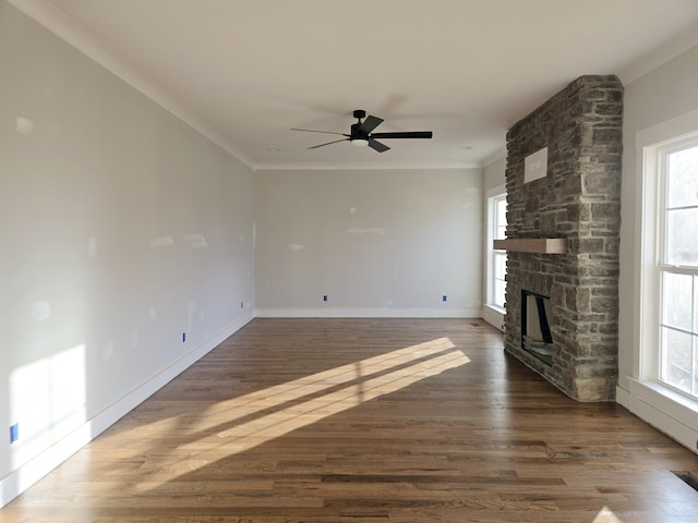 unfurnished living room featuring ornamental molding, a stone fireplace, dark wood-type flooring, and a healthy amount of sunlight