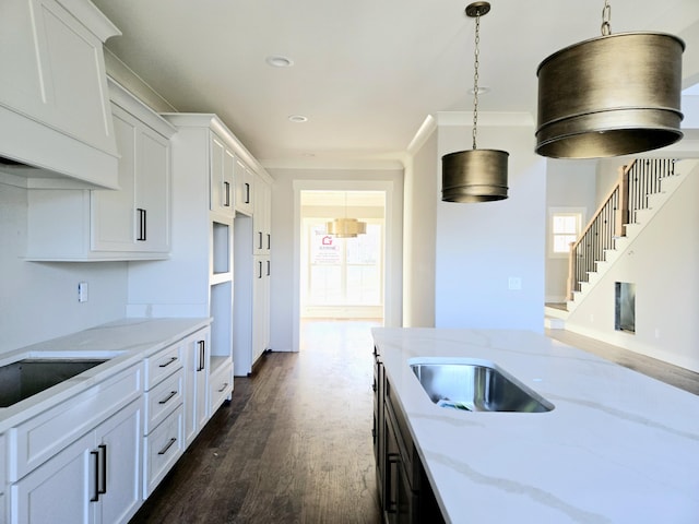 kitchen with dark hardwood / wood-style floors, light stone counters, ornamental molding, white cabinets, and decorative light fixtures