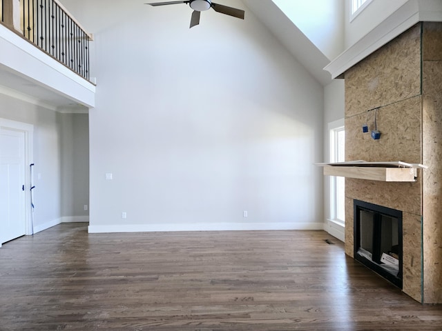 unfurnished living room featuring ceiling fan, a towering ceiling, dark hardwood / wood-style flooring, and a fireplace