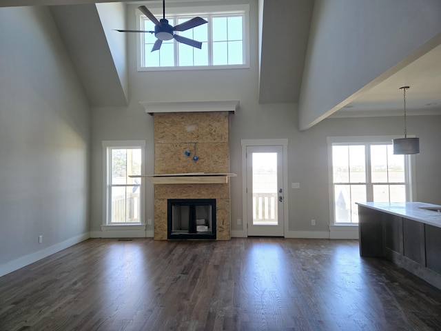 unfurnished living room featuring dark hardwood / wood-style flooring, ceiling fan, a tiled fireplace, and a healthy amount of sunlight