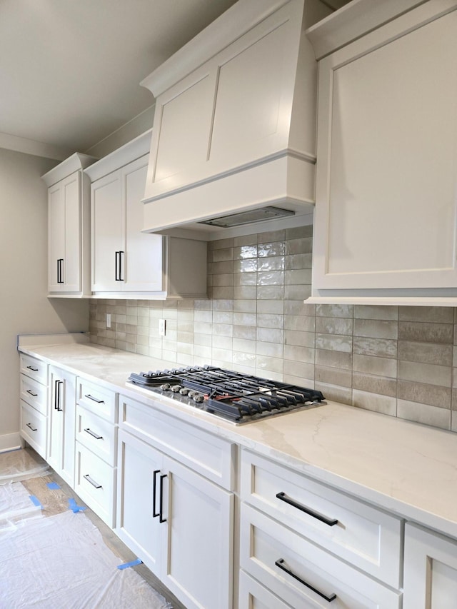 kitchen featuring backsplash, light stone counters, white cabinets, custom exhaust hood, and stainless steel gas stovetop