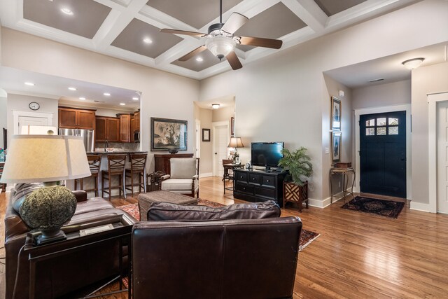 living room featuring wood-type flooring, ceiling fan, coffered ceiling, beamed ceiling, and a high ceiling