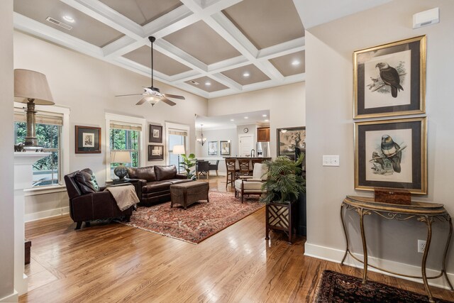 living room featuring ceiling fan, coffered ceiling, wood-type flooring, and beam ceiling