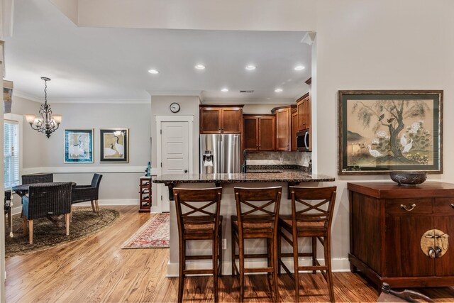 kitchen with a breakfast bar area, light hardwood / wood-style flooring, hanging light fixtures, stainless steel appliances, and a chandelier