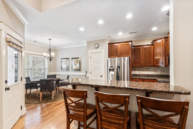 kitchen featuring stainless steel fridge with ice dispenser, a chandelier, light wood-type flooring, ornamental molding, and decorative light fixtures