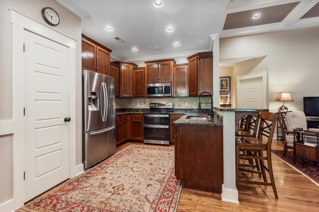 kitchen featuring sink, kitchen peninsula, light hardwood / wood-style floors, stainless steel appliances, and a breakfast bar area