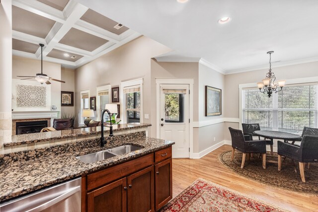 kitchen with sink, ceiling fan with notable chandelier, dark stone counters, stainless steel dishwasher, and light hardwood / wood-style flooring