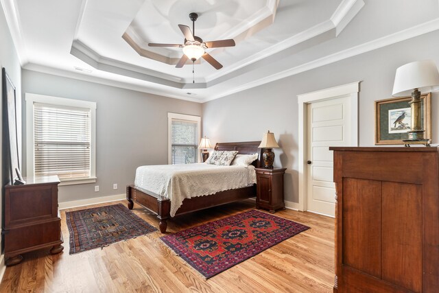 bedroom featuring ornamental molding, a raised ceiling, light wood-type flooring, and ceiling fan