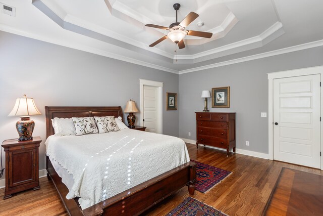 bedroom with ornamental molding, a raised ceiling, hardwood / wood-style flooring, and ceiling fan