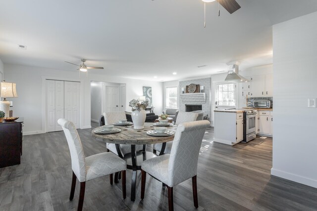 dining space with dark wood-type flooring, ceiling fan, and a brick fireplace