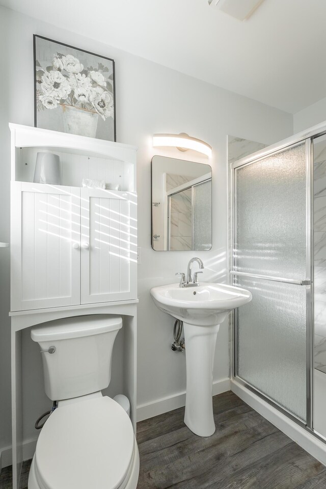 bathroom with wood-type flooring, a shower with shower door, and toilet