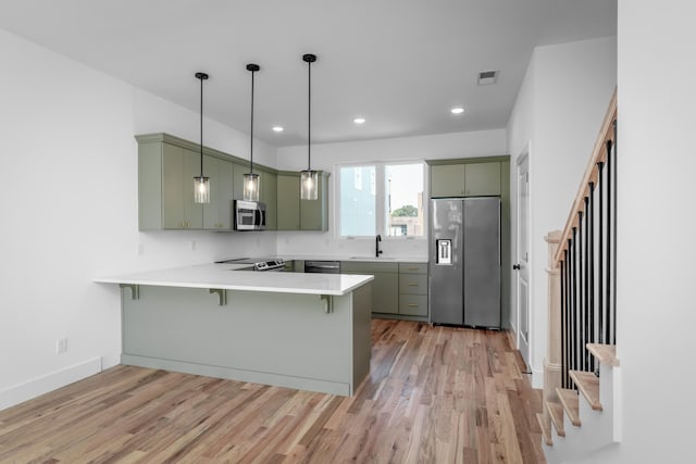 kitchen with light wood-type flooring, kitchen peninsula, stainless steel appliances, green cabinets, and a kitchen bar