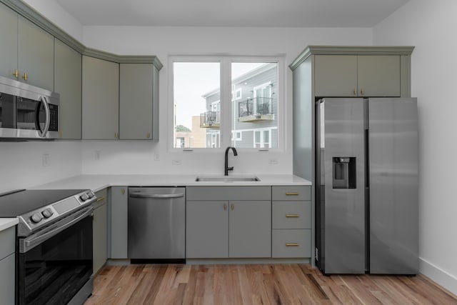 kitchen with appliances with stainless steel finishes, gray cabinetry, sink, and light hardwood / wood-style flooring