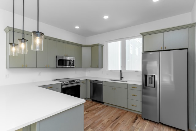 kitchen featuring light hardwood / wood-style floors, sink, kitchen peninsula, hanging light fixtures, and stainless steel appliances