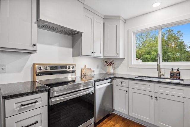 kitchen with dark stone counters, appliances with stainless steel finishes, sink, and dark hardwood / wood-style flooring