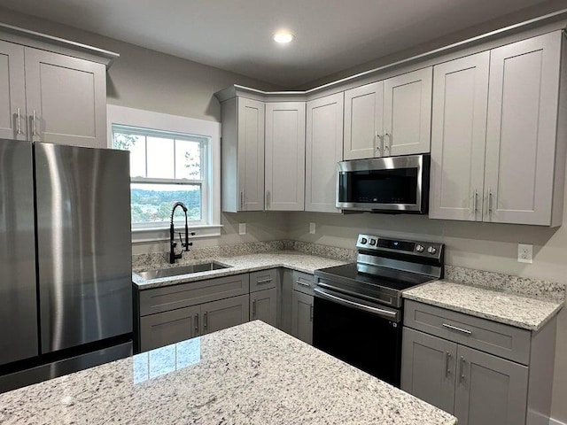 kitchen with gray cabinetry, light stone counters, sink, and stainless steel appliances