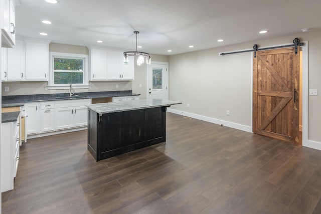 kitchen with a barn door, decorative light fixtures, a kitchen island, white cabinets, and sink